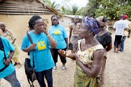  Einige Mitarbeiterinnen des Teams von Medica Liberia diskutieren in einer liberianischen Dorfgemeinde miteinander. Sie tragen blaue T-Shirts mit dem Aufdruck „medica mondiale“. 