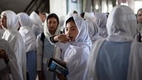 Gruppe Schülerinnen einer Mädchenschule in Afghanistan, mit weißen Kopftüchern. Zwei Mädchen blicken mittig in die Kamera und halten Bücher in den Händen