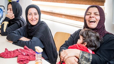 Zwei Teilnehmerinnen eines Nähkurses im Irak blicken lachend in die Kamera    