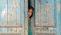 Ein Mädchen schaut vorsichtig aus einer Türe, die nur einen Spalt weit geöffnet ist.