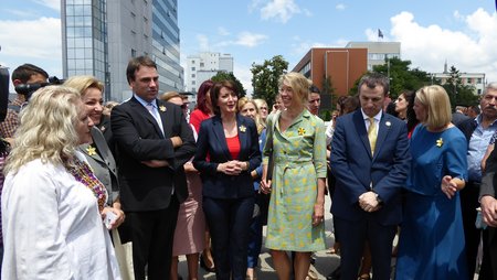  A number of people gathered at a public location in Pristina. They are dressed smartly and each is wearing a badge in the design of a yellow flower.