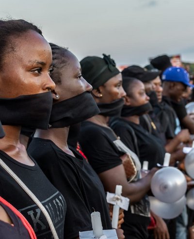 A long row of women at a demonstration in Liberia. They are standing side-by-side, their mouths are covered with a black cloth and they are holding candles.