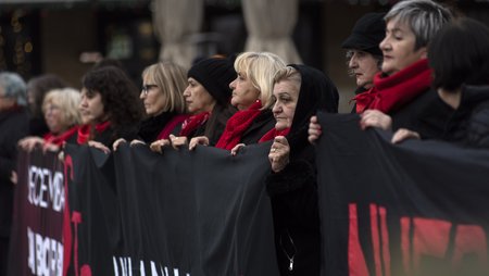 Zu sehen sind zahlreiche, in schwarz und rot gekleidete Frauen auf einer Demonstration. Sie stehen in einer Reihe und halten ein Demobanner. Die Aufschrift ist nicht zu erkennen. 