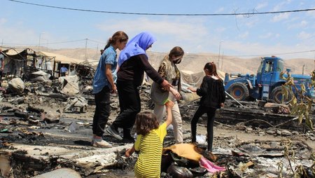 Frauen und Mädchen bahnen sich ihren Weg durch die Trümmer eines durch Brand zerstörten Geflüchtetenlagers im Nordirak. 