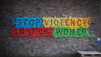 The wall of a house with many little colourful origami birds stuck on it forming the slogan: Stop violence against women. 