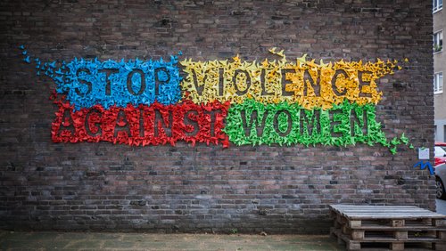 The wall of a house with many little colourful origami birds stuck on it forming the slogan: "Stop vilence against women."