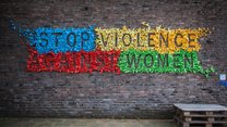 The wall of a house with many little colourful origami birds stuck on it forming the slogan: Stop violence against women.