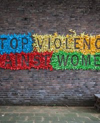 Ein aus bunten Origami-Vögeln gebastelter Schriftzug an einer Hauswand: Stop violence against women