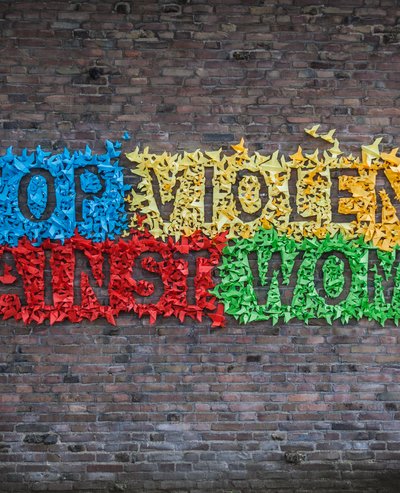 The wall of a house with many little colourful origami birds stuck on it forming the slogan: Stop violence against women. 