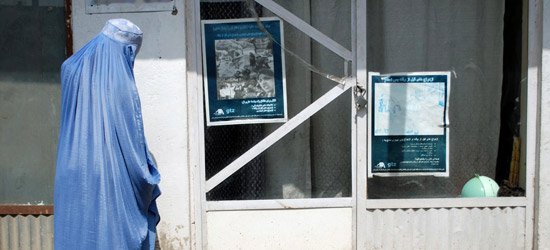 Eine Frau in einer blauen Burka vor einer Glastür an der ein Informationsplakat in arabischer Schrift hängt.