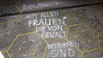 Auf einem Straßenpflaster steht ein Kreidespruch "Solidarität mit allen Frauen*, die von Gewalt betroffen sind"