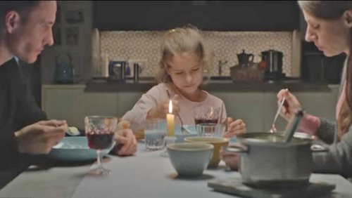 Eine Familie sitzt am Essenstisch: Links der Vater, in der Mitte ein kleines Mädchen, rechts die Mutter.