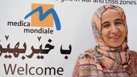 Zu sehen ist das Logo der Frauenrechtsorganisation medica mondiale im Hintergrund mit arabischen Schriftzeichen darunter. Rechts davor das Gesicht einer freundlich lächelnden Frau. Es ist Rechtsberaterin Jihan Abas Mohammed. 