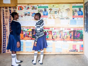 Two girls in school uniform look at several sex education posters displayed on a wall.