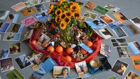 Arrangement von Blumen, Tüchern, Anti-Stress-Bällen und Fotos auf dem Boden. 
