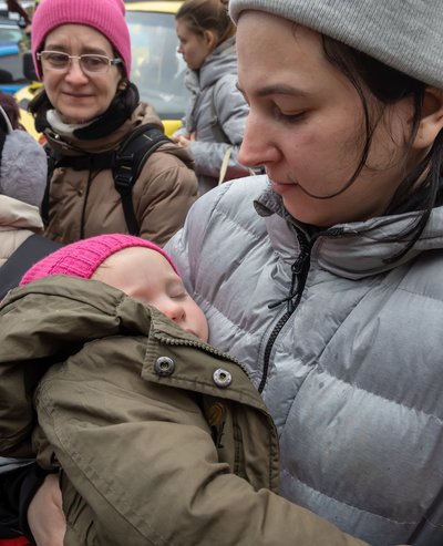 Eine Ukrainerin hält ein Kleinkind auf dem Arm, im Hintergrund sind weitere Geflüchtete zu sehen.