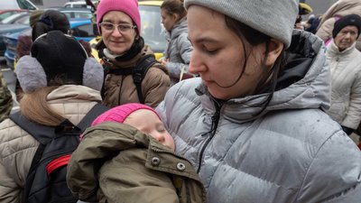 A Ukrainian woman is holding a small child in her arms. In the background we see more refugees.