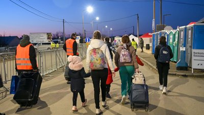 People fleeing from Ukraine. There are many women and children with baggage, as well as people wearing high-visibility vests. 