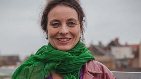 A woman with a green scarf looks into the camera