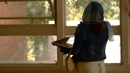 Eine Mitarbeiterin hält einen Laptop auf dem Arm und blickt mit dem Telefon am Ohr aus dem Fenster. 