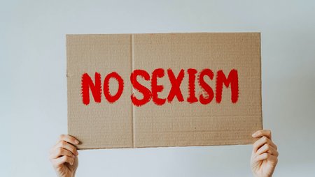 Two hands holding a sign with the message, “No Sexism”