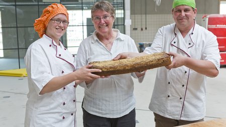 Drei Personen in Kochkleidung halten ein Brot