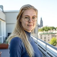 Eine Frau in einem blauen Rollkragenpullover steht auf einer Dachterrasse mit Kölner Dom im Hintergrund. Es ist Helena Haack, Pressereferentin bei medica mondiale.