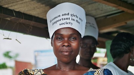 A woman is carrying a sign on her head with the words “Women and girls are important in the society”.