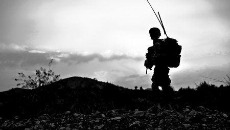 Ein im Gegenlicht fotografiertes Schwarz-Weiß-Foto mit der Silhouette eines Soldaten ist auf einem Hügel.