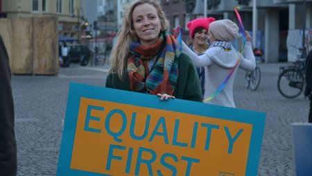 A woman is holding a sign from medica mondiale with the slogan “Equality first”.