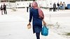 Frau aus Afghanistan mit Plastikbeuteln in der Hand läuft durch ein Geflüchtetenlager