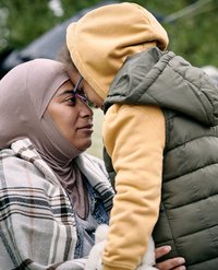 Eine Frau mit Kopftuch hält ihre Tochter und lehnt ihre Stirn an das Gesicht ihrer Tochter.