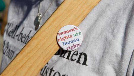 A badge with the slogan “women’s rights are human rights” with each word in a different colour.