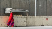 Eine Frau mit rotem Schleier läuft an einer Betonmauer mit Stacheldraht entlang in Kabul Afghanistan. 