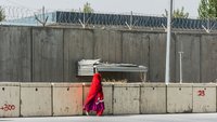 Eine Frau mit rotem Schleier läuft an einer Betonmauer mit Stacheldraht entlang in Kabul Afghanistan. 