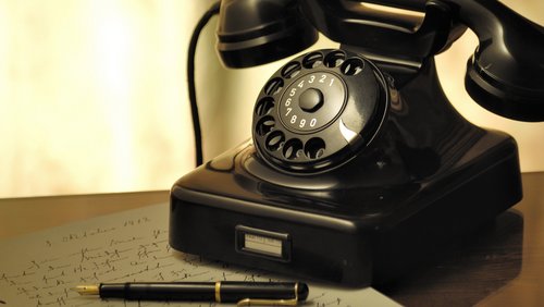Altes Telefon steht auf dem Tisch mit Notizblock und Stift