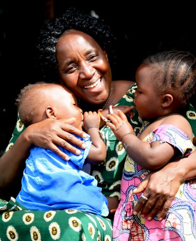 Eine lachende Frau hält zwei kleine Kinder im Arm. 