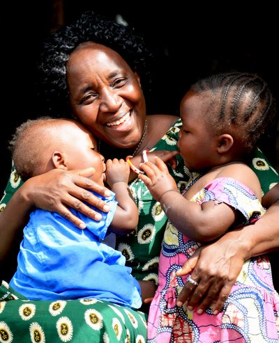 Eine lachende Frau hält zwei kleine Kinder im Arm. 