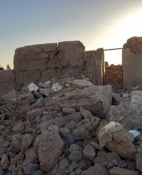 Steine stapeln sich, ein zerstörtes Haus im Hintergrund