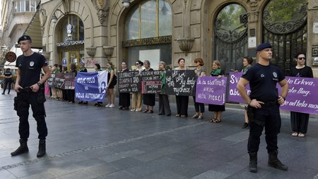 Dozens of women are standing in a row holding placards in front of a public building. In the foreground there are two police officers.