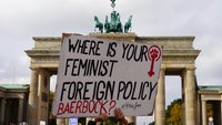 Ein Demonstrationsplakat wird vor dem Brandenburger Tor in die Höhe gehalten. Aufschrift: Where is your feminist foreign policy, Baerbock? #MahsaAmini