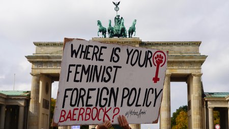 Ein Demonstrationsplakat wird vor dem Brandenburger Tor in die Höhe gehalten. Aufschrift: Where is your feminist foreign policy, Baerbock? #MahsaAmini