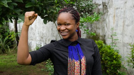 A woman raising her fist in a feminist way looks smilingly into the camera