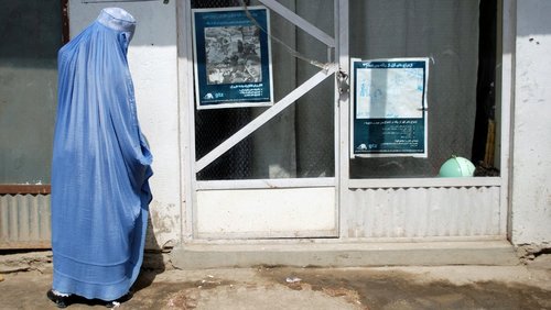 Eine Frau in einer blauen Burka vor einer Glastür an der ein Informationsplakat hängt.