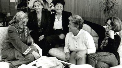 Schwarz-weiß Foto von Sabiha Husic und weiteren Frauen des Medica Zenica Teams im Jahr 1997, die Frauen sitzen auf mehreren Sesseln und lachen.