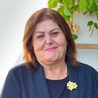 Eine Frau steht vor einer Häuserwand und lächelt in die Kamera. Es ist Dr. Bayan Kader Rasul, Mitbegründerin der nordirakischen Frauenrechtsorganisation EMMA.